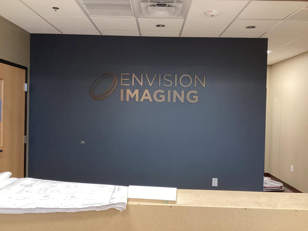 Reception area with a blue accent wall displaying the ENVISION IMAGING logo in metallic letters; a counter with papers sits in the foreground.