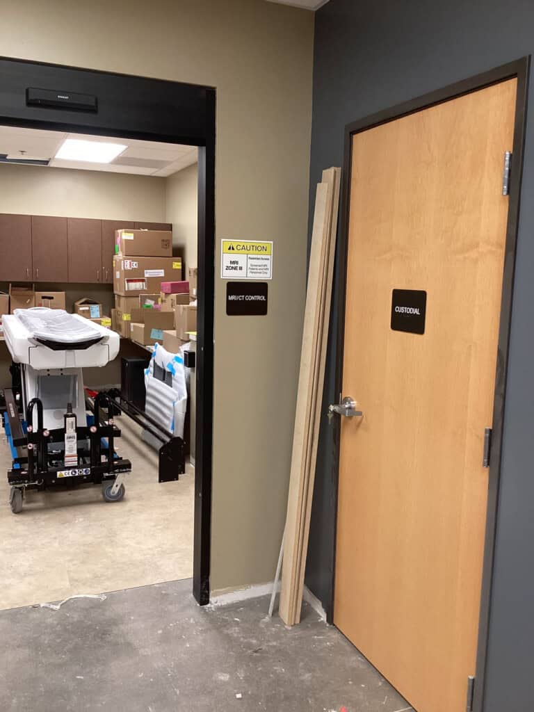 A storage room with boxes and equipment is visible through an open door labeled “Robot Control.” Next to it, a closed door labeled “Custodial” has wooden planks leaning against the wall.