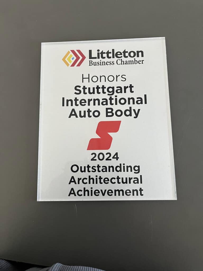 A plaque from Littleton Business Chamber honoring Stuttgart International Auto Body for 2024 Outstanding Architectural Achievement, placed on a dark surface.