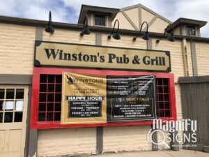 The exterior of Winstons Pub & Grill, featuring a large sign above the entrance and a banner advertising happy hour deals and drink specials, mounted on a beige brick building.