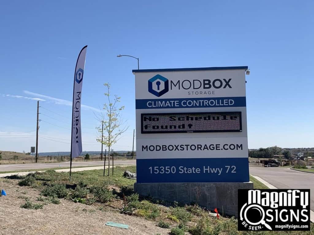 Outdoor sign for MODBOX Storage displays Climate Controlled and No Schedule found. The sign includes the website, address (15350 State Hwy 72), and Magnify Signs branding in the lower right corner.