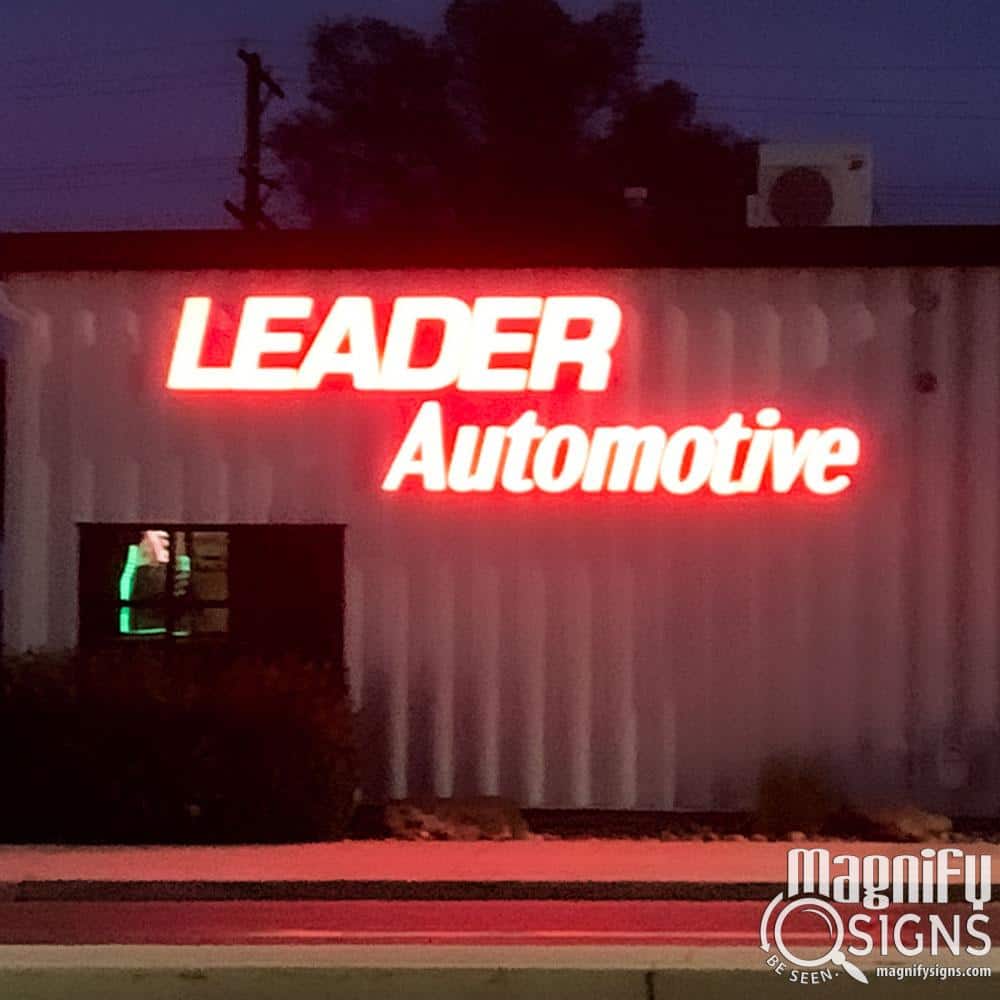 A brightly lit red neon sign reads LEADER Automotive on the side of a building at night, with the logo Magnify Signs visible in the bottom right corner.