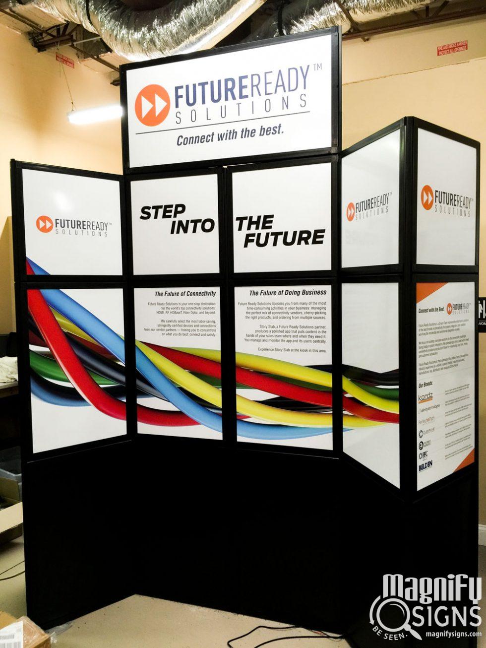 A trade show display for FutureReady Solutions features the slogan “Step Into the Future” with colorful cables flowing across the panels and informational text. Magnify Signs logo appears in the bottom right corner.